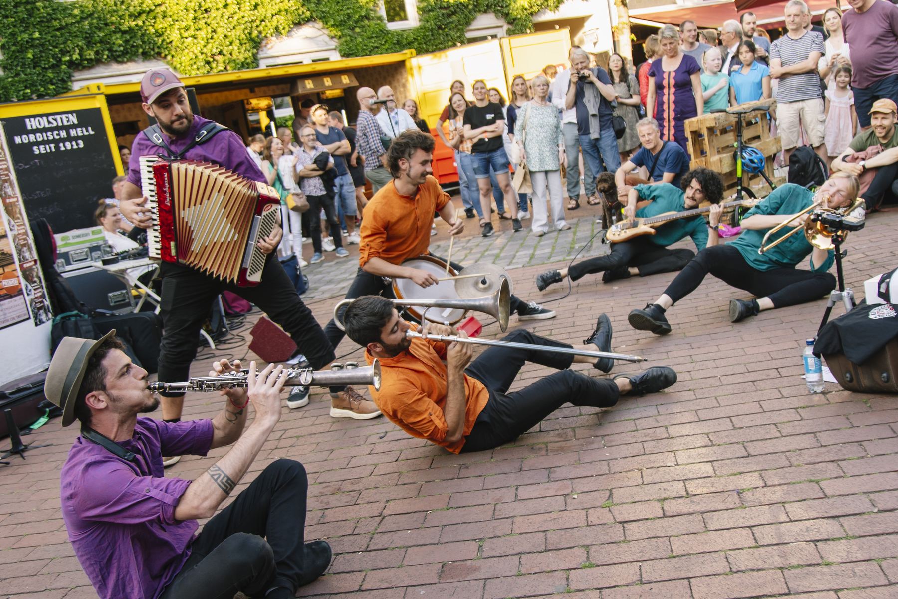 Desmadre Callejero playing in the street, musicians on the ground and the crowd gathered around